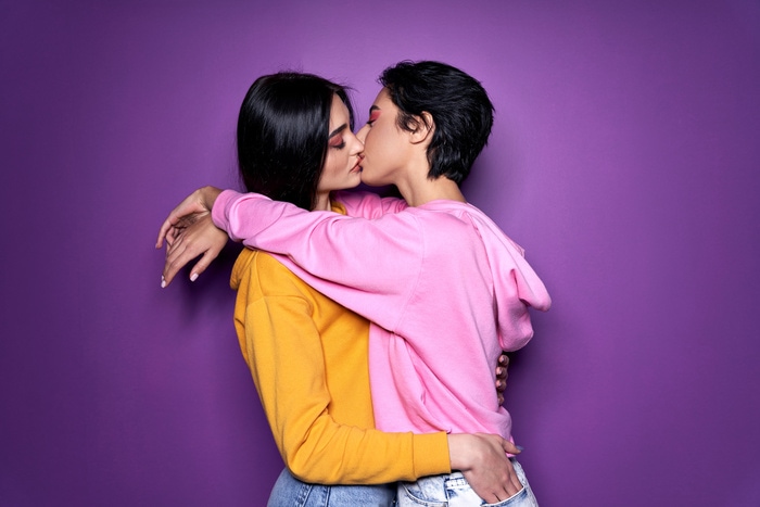 best LGBTQ dating apps - Two pretty sexy stylish cool generation z girls lgbtq lesbian couple dating in love hugging enjoying intimate tender sensual moment together kissing with eyes closed isolated on purple background